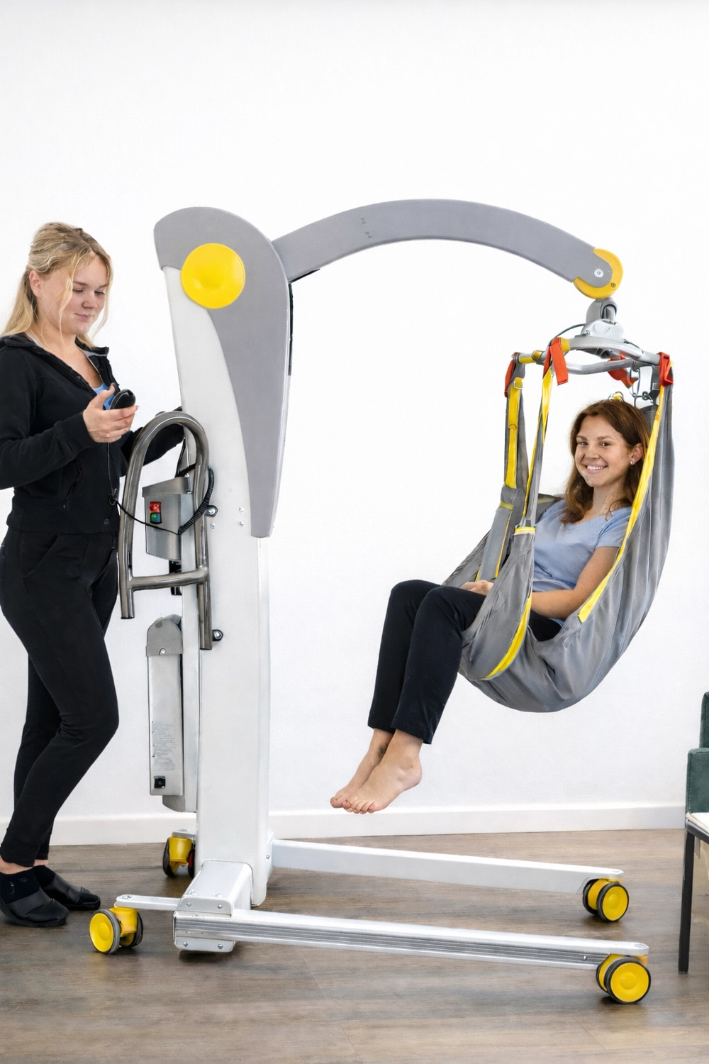 Hadzsi GbR - Assistenzdienstleistungen - Ein behindertes Mädchen wird mithilfe eines mobilen Patientenlifters vom Typ Handi-Move Victor mit Sitzgurt angehoben.